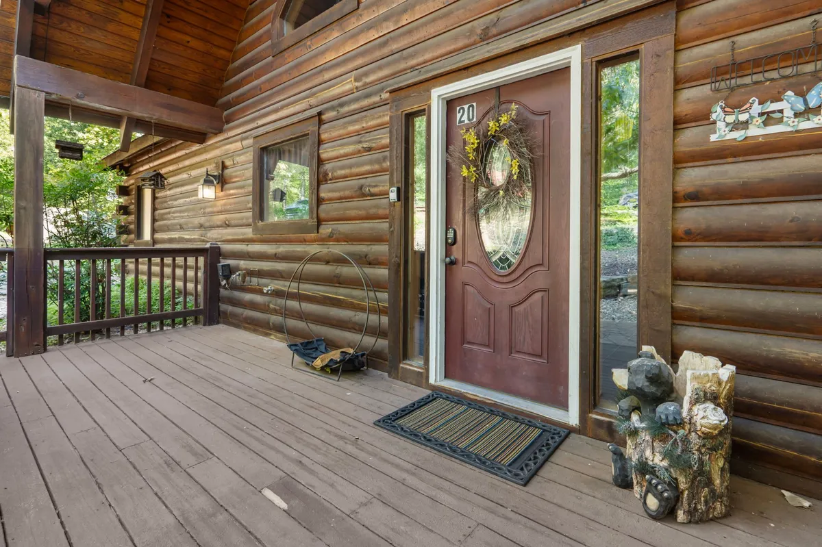 This exterior shot features the front facade of the Ole Hickory log cabin, highlighting a welcoming front door adorned with a decorative wreath, a wooden porch, and natural stone accents. The inviting atmosphere suggests a comfortable home base for travelers.