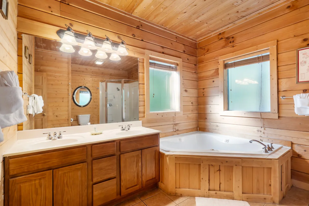 A spacious ensuite bathroom with a double sink vanity, a luxurious jacuzzi tub, a separate shower stall, and large windows that draw in natural light. The scene highlights the spa-like comfort and the opportunity for a soothing soak after a busy day.