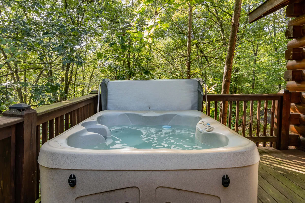 A peaceful scene featuring a hot tub on a wooden deck, bordered by sturdy railing and surrounded by tall trees. The area invites relaxation and offers privacy, with forest views in every direction.