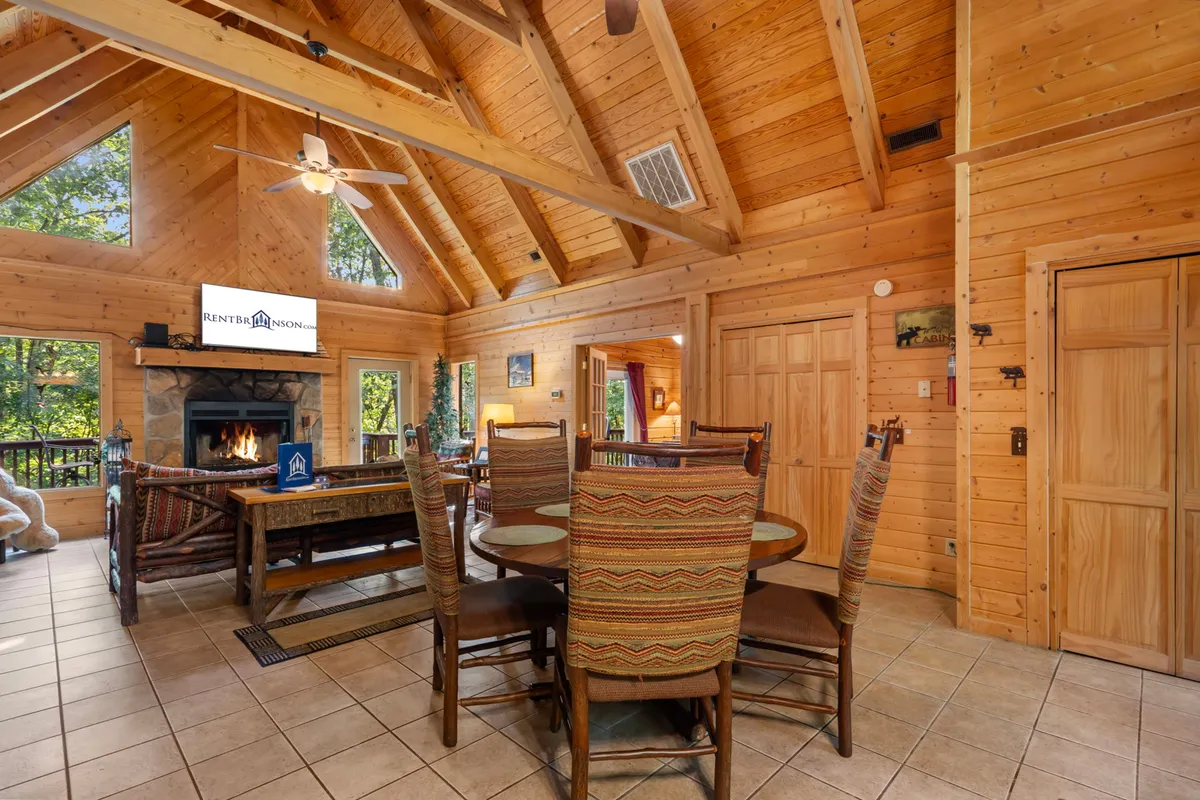 An open-concept dining and living area with a long dining table, fireplace, large windows, and a TV. The space is ideal for family dinners, game nights, and movie evenings.
