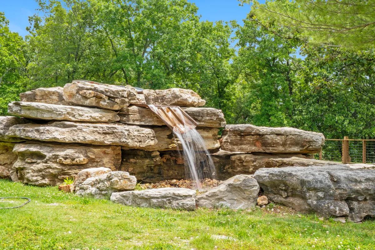 A peaceful natural stone waterfall nestled amidst lush greenery and vibrant grass, creating a tranquil spot perfect for relaxation and quiet reflection. The setting is untouched by construction, emphasizing the natural beauty and serenity of the resort landscape.