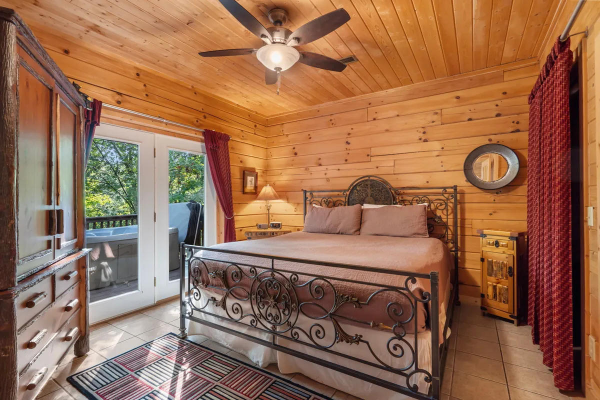 A master bedroom with an iron bed frame, wooden walls, and a window draped to let in soft natural light. The nightstand and lamp beside the bed add a touch of warmth, making the space feel both private and welcoming.