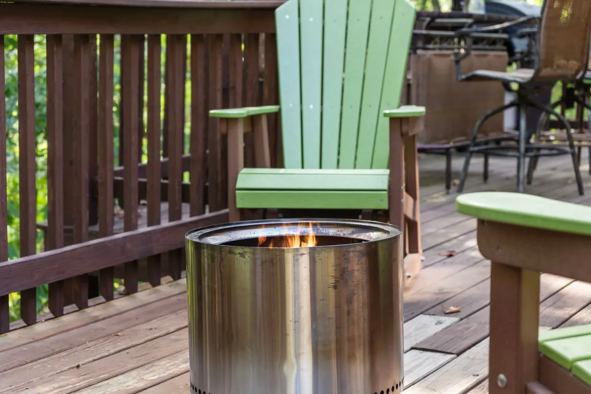 This image features a cozy fire pit surrounded by green Adirondack chairs on a wooden deck, set against the backdrop of greenery. The inviting setup is ideal for relaxing after a day outdoors, with space for both people and pets to unwind together under the stars.