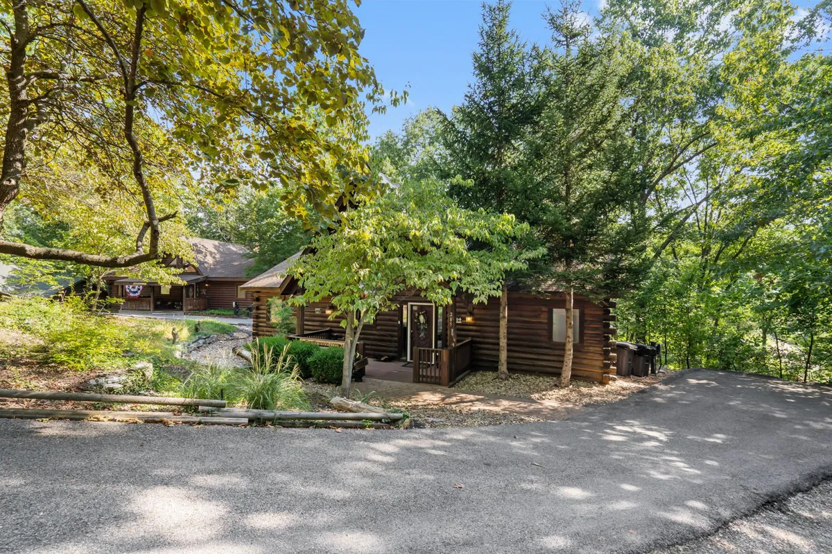 A log cabin surrounded by lush greenery, with a pathway leading up to the front porch and decorative planters accenting the entrance. The architecture exudes rustic charm and seclusion, with ample space for outdoor relaxation and privacy.