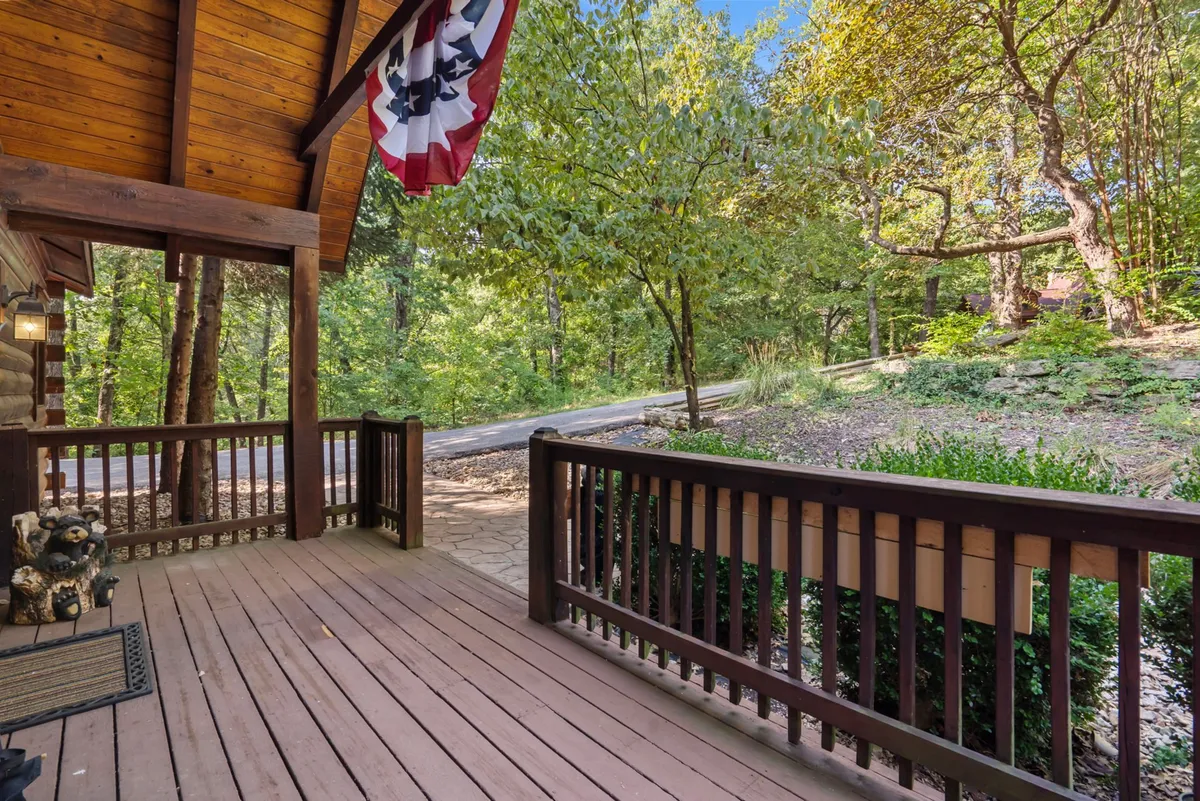 A welcoming wooden porch adorned with an American flag, set against a backdrop of abundant greenery. The porch overlooks a leafy, serene landscape, inviting guests to relax outdoors and enjoy the setting's seclusion.